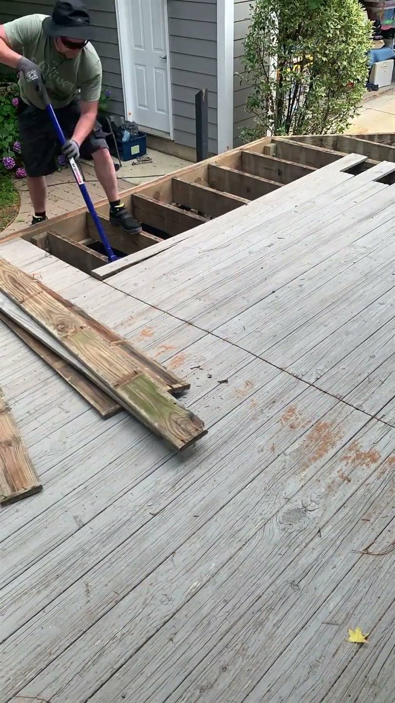 Old deck boards being prised up with a bar, the joists beneath already exposed