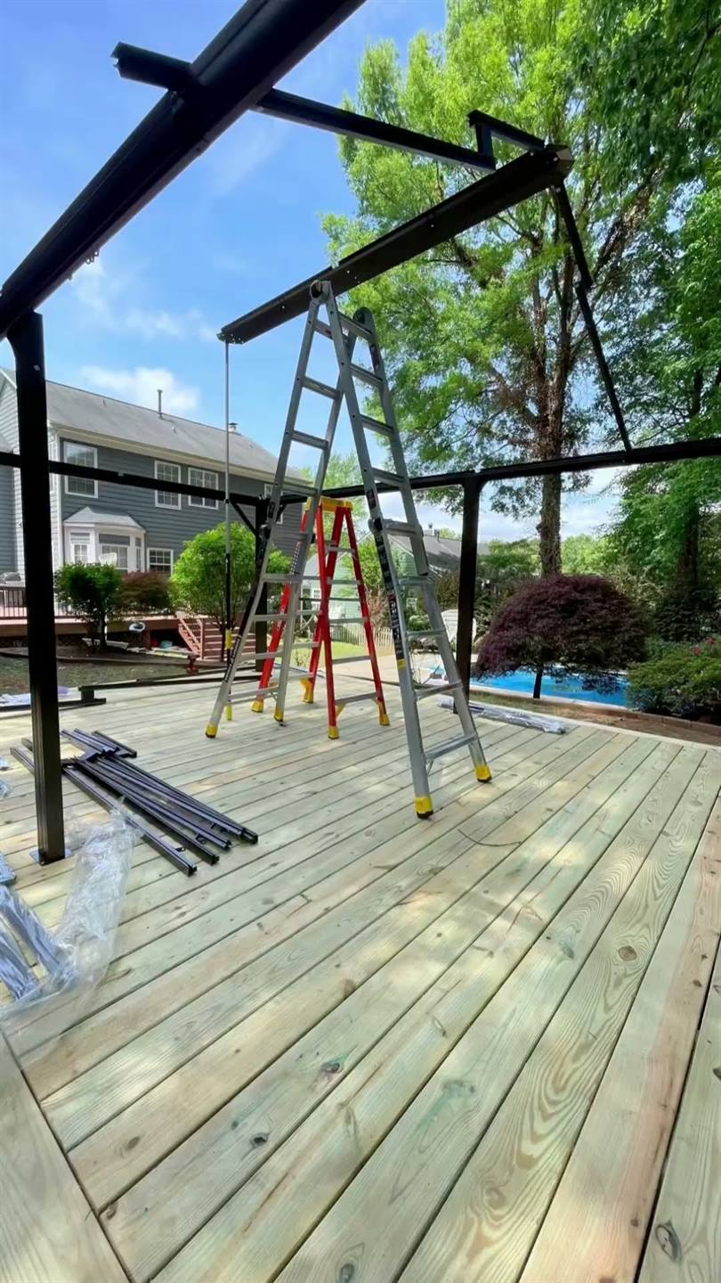A new timber deck with the dark frame of a gazebo being raised above it and ladders standing on the boards