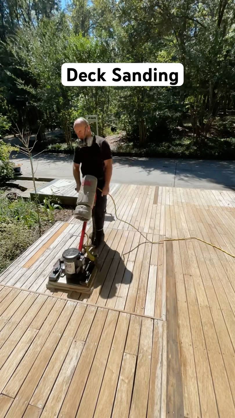 A worker running a floor sander across the boards of a large timber deck on a bright day