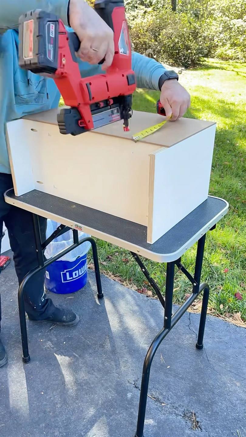A white cabinet carcass being fixed together with a nail gun on a folding table outdoors