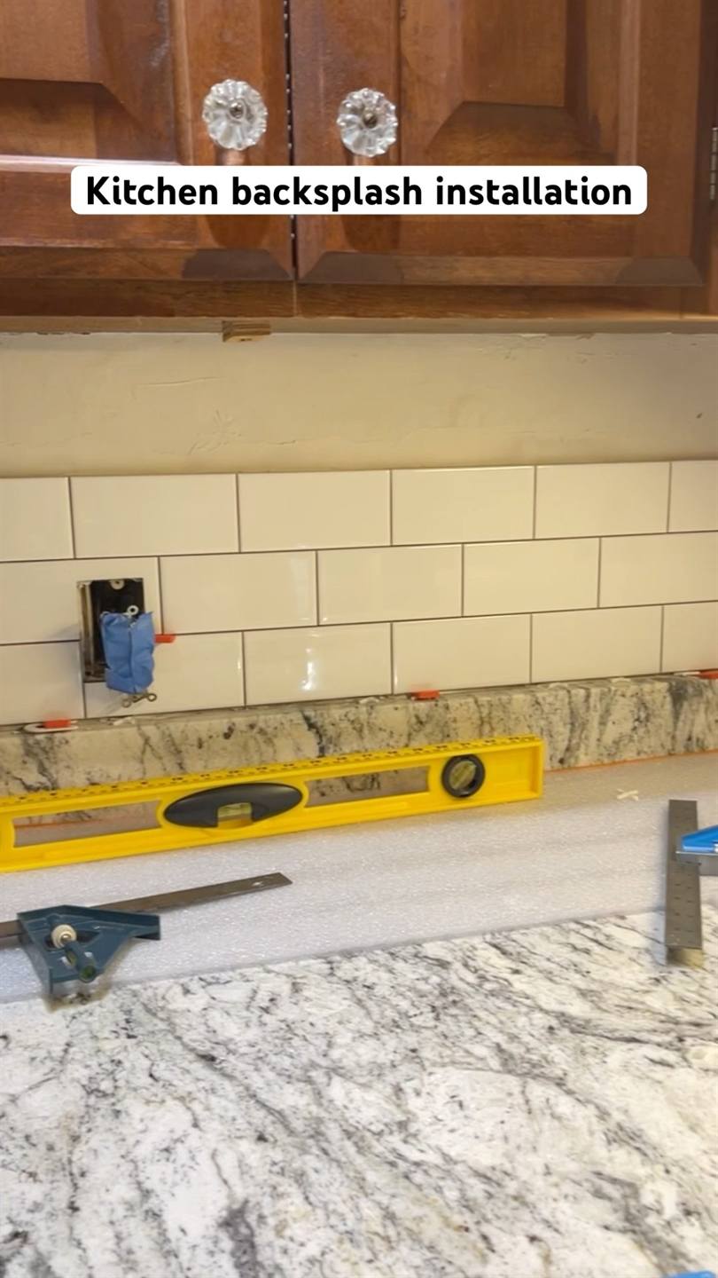 Cream subway tile set in courses above a granite counter, with a spirit level and a combination square resting on the worktop