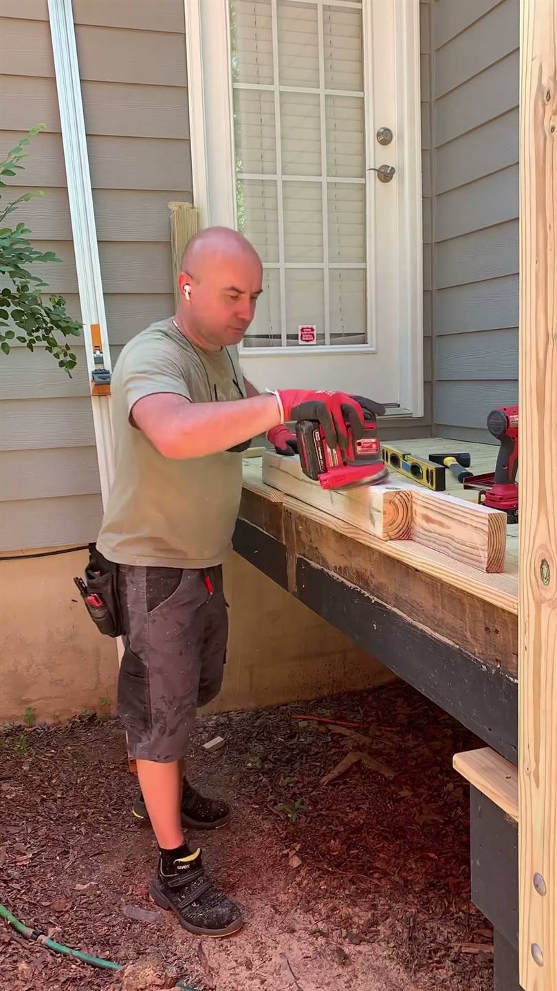 A worker cutting rail timber with a saw on a deck beside the posts already standing