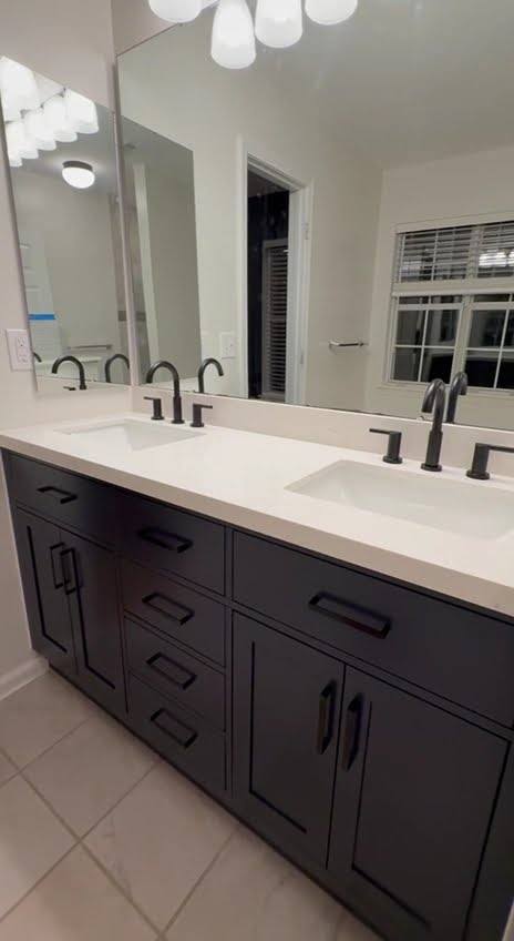 A dark double vanity with a white counter, black taps and two lit mirrors above it