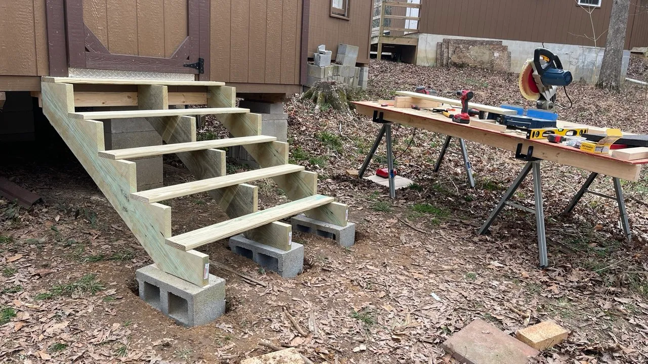 Stair treads being fitted to the stringers beside a work bench and mitre saw