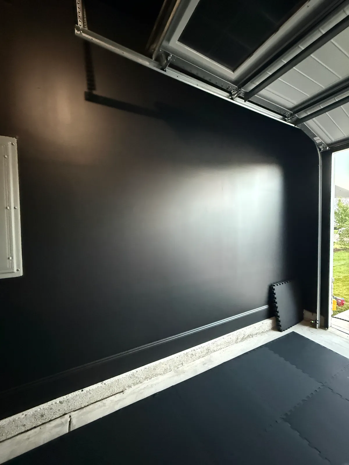 Dark garage wall and tiled floor with the sectional door open to daylight