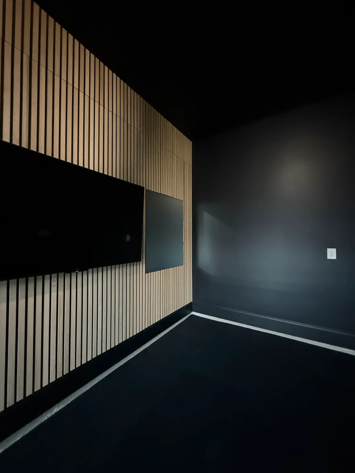 Wood slat wall meeting a dark painted wall in low light