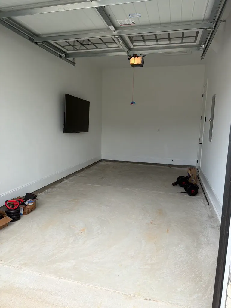 White garage interior with a wall-mounted television and bare concrete floor