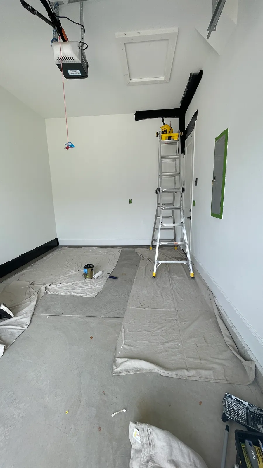 Garage with drop cloths on the floor, a stepladder, and dark trim being installed