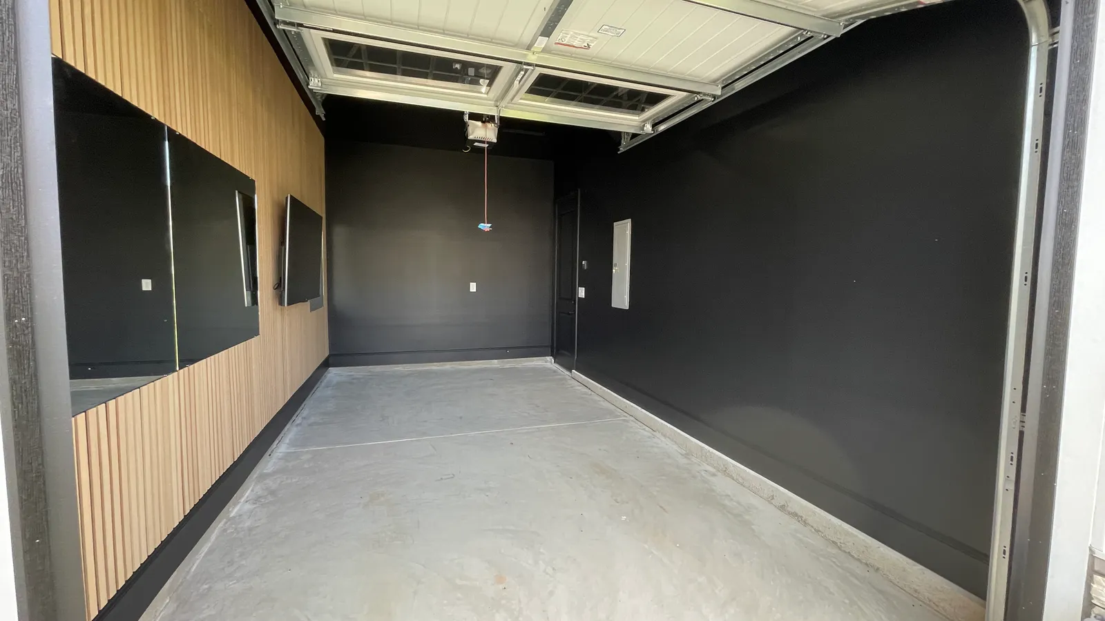 Garage with finished slat wall and dark walls but a bare concrete floor