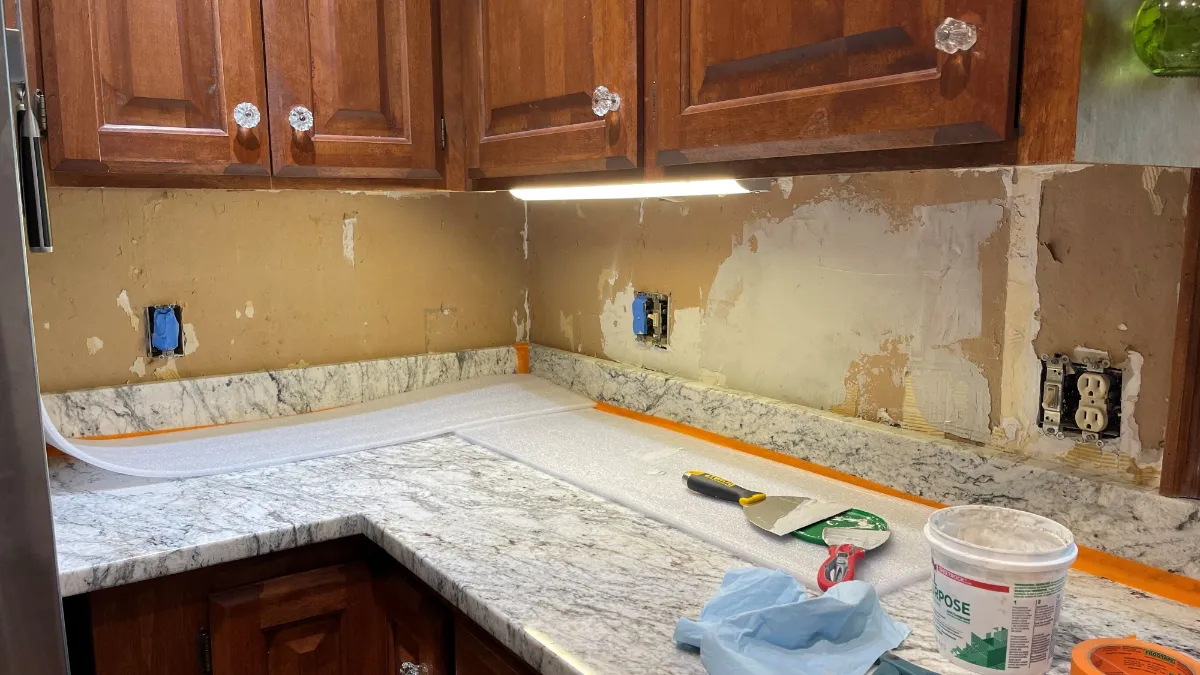 The backsplash wall stripped to bare plaster above the granite, the worktop papered over and taped