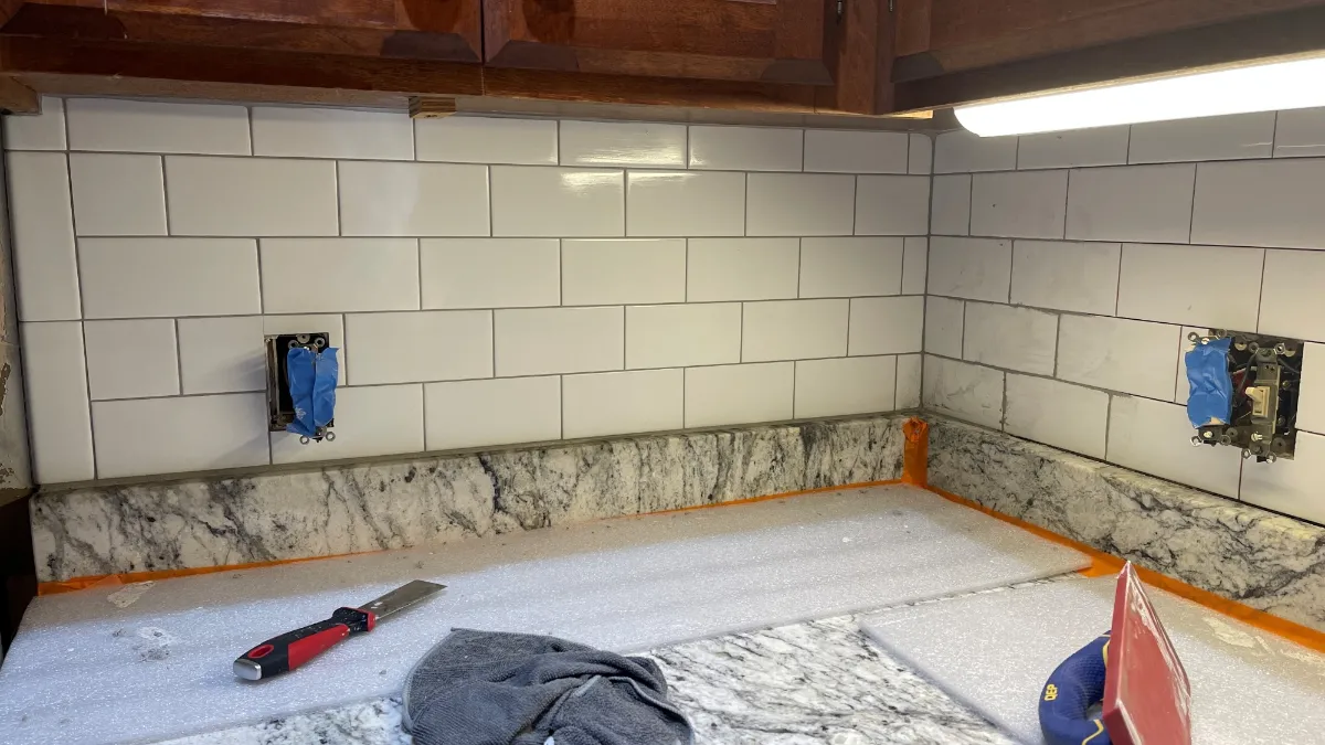 The tiled run reaching the wall cabinets and cut around the outlets, still ungrouted