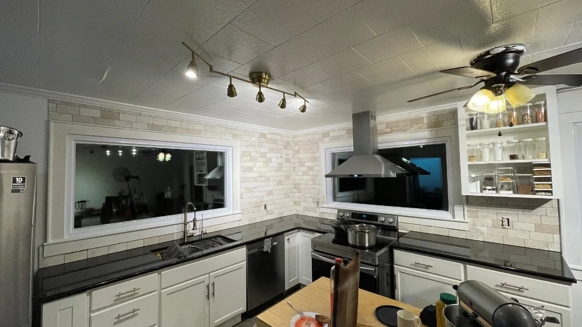 The finished kitchen from the doorway: travertine carried to the ceiling behind the hood, open shelving, and track lighting