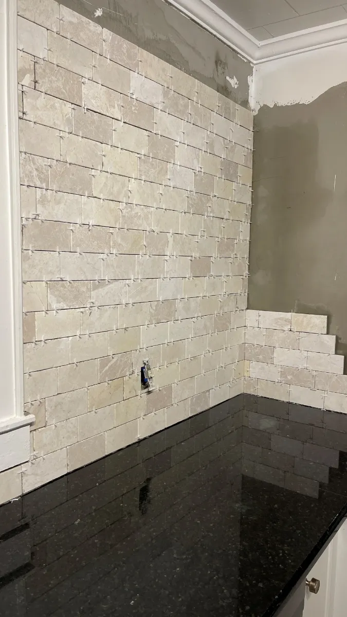 Travertine set part-way up the range wall above the black granite, the plaster above it still bare