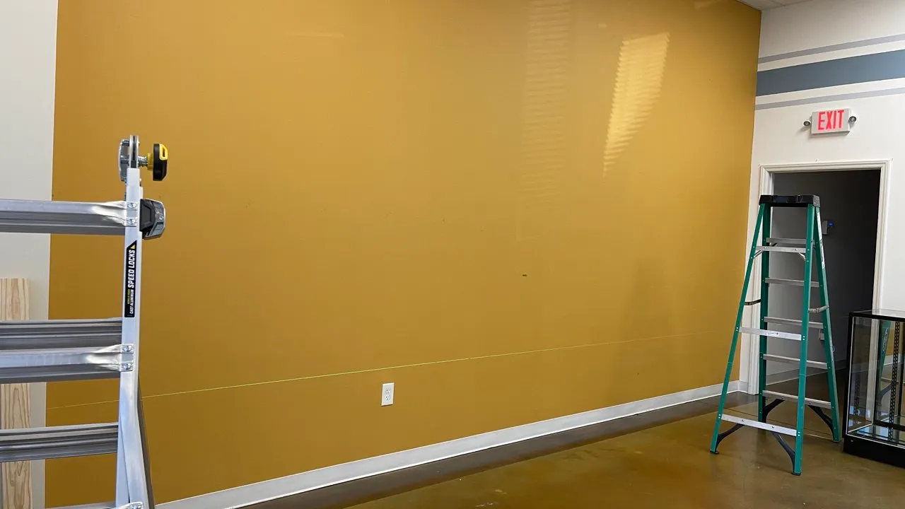 Plain yellow commercial wall with stepladders in front of it and an exit sign to the right