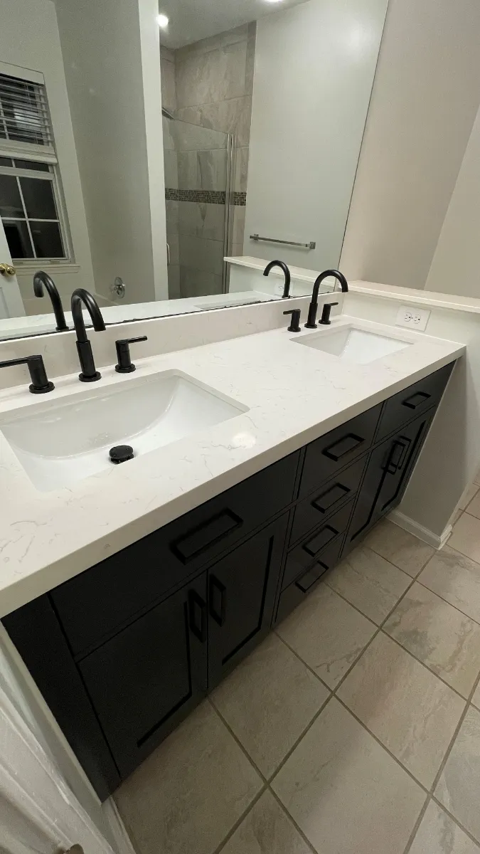 A dark timber double vanity with a white top and black taps below a wide mirror