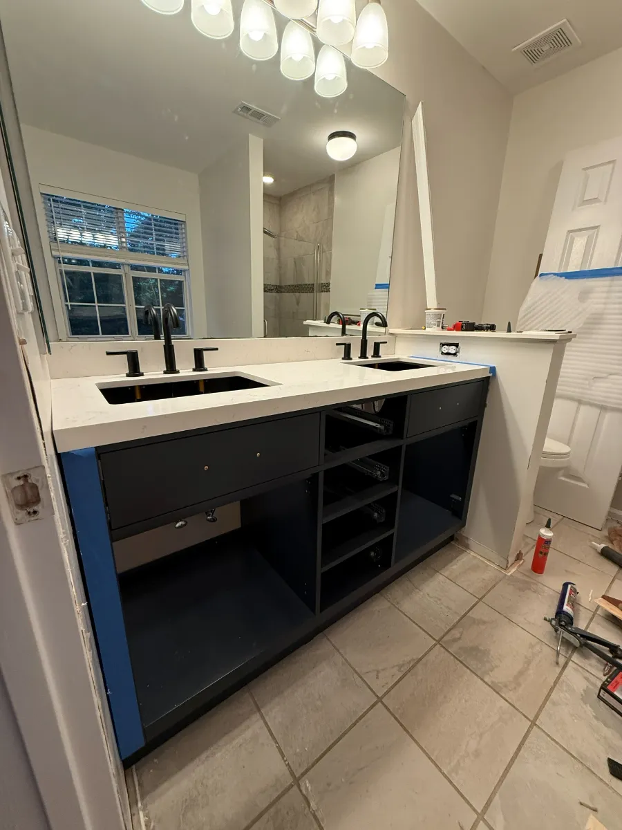 A navy double vanity with a white counter, black taps, and lit mirrors above it
