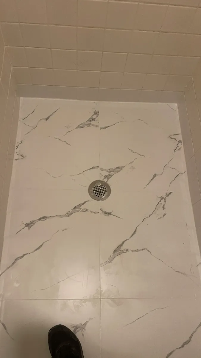 Large marble-patterned tile laid to a shower floor and falling to a central drain