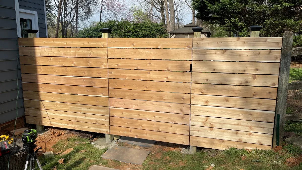 A horizontal cedar privacy screen built between posts along the side of a house