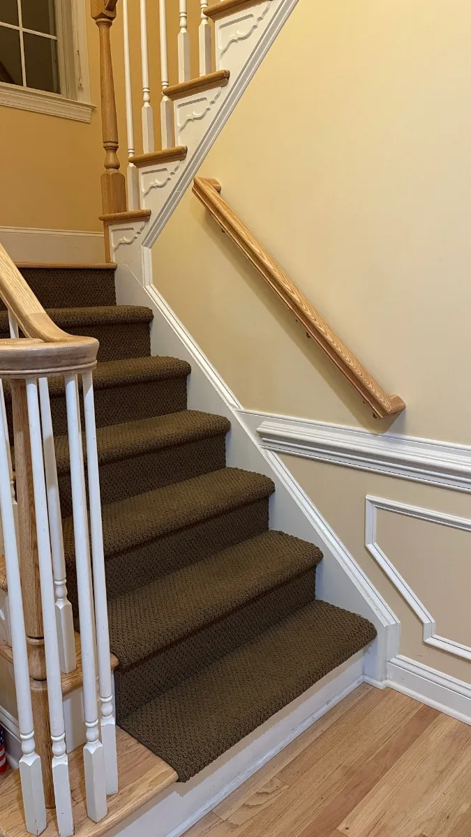 An oak handrail running the wall of a carpeted staircase beside white balusters