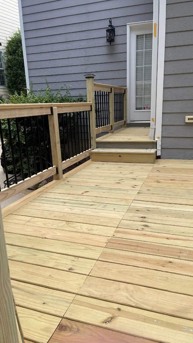 A new timber deck with black metal balusters and wide stairs down to a paved path