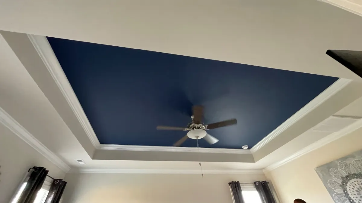 A tray ceiling painted deep navy inside white crown molding, with a ceiling fan at its center