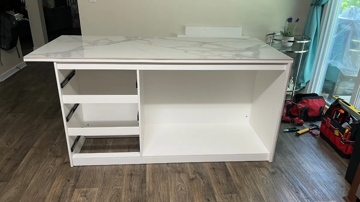 The white island carcass standing open on the floor, shelving and drawer bank in place before the top goes on