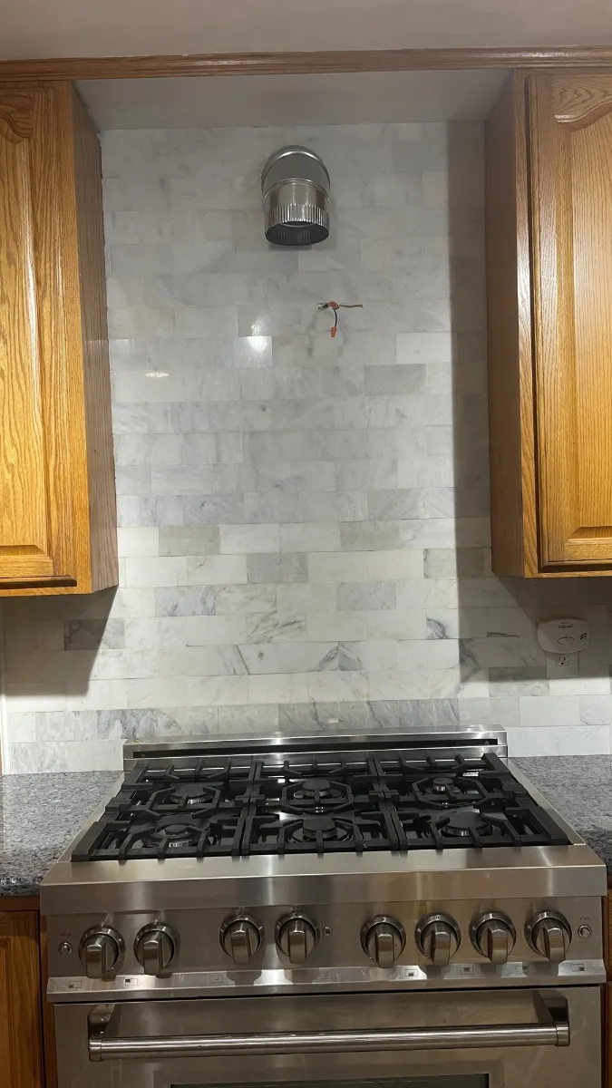 Marble tile carried up the range wall behind a stainless gas range, between oak wall cabinets