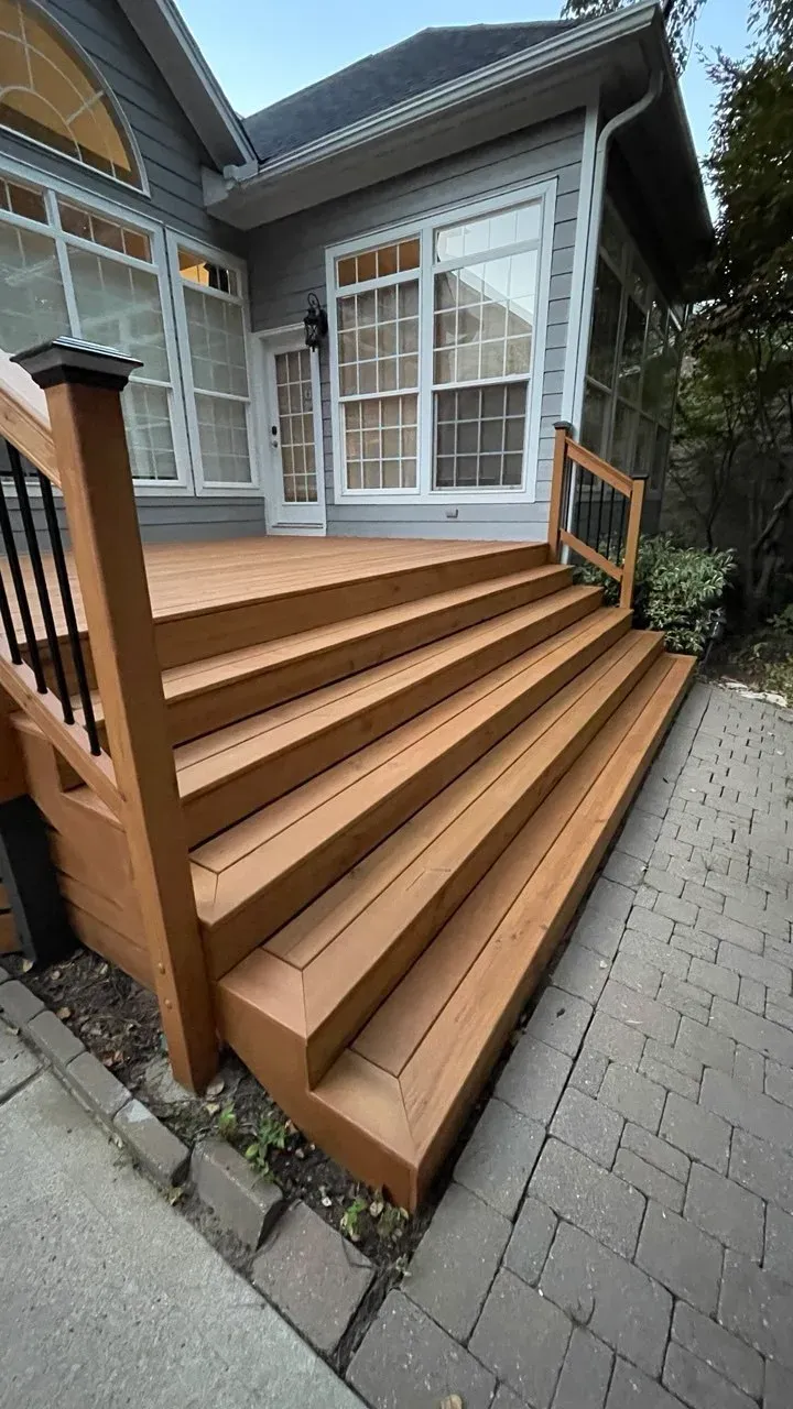 Finished wide composite deck stairs with a dark balustrade beside a paved path